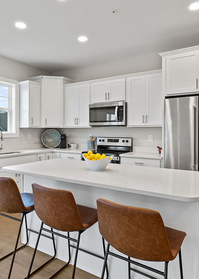 Bright, modern kitchen showcasing sleek white cabinetry, a stylish island with seating, and stainless steel appliances.