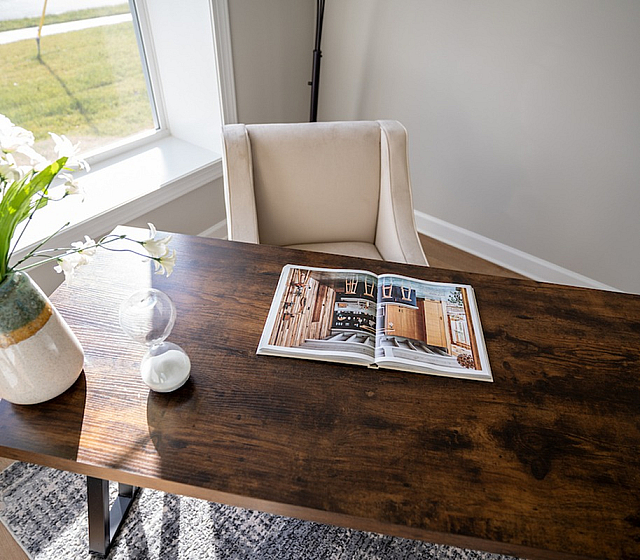 Bright and elegant home office with a wooden desk, chic beige chair, and decorative vase set by a sunlit window.
