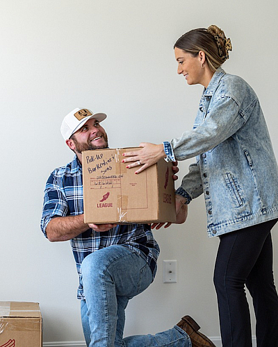 Cheerful couple settling into their new home, sharing a moment of teamwork while unpacking cardboard boxes on a stylish hardwood floor.