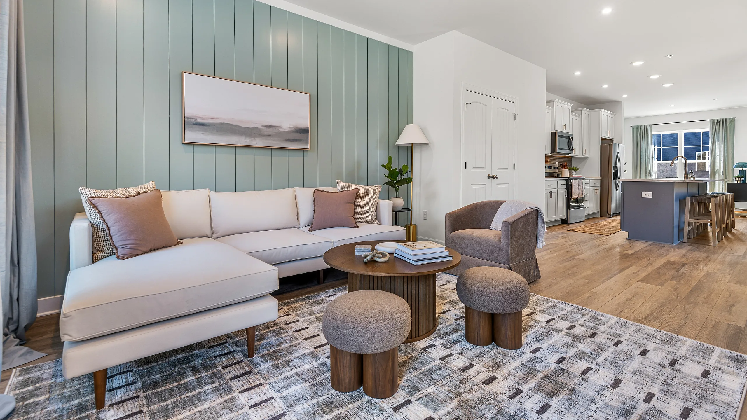 Chic and modern open-concept living space with elegant light wood flooring, featuring a plush sectional sofa, stylish armchair, and sleek kitchen with a large island.