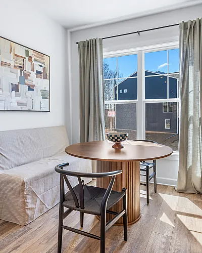 Charming dining nook with natural light, featuring a round wooden table, cozy seating, and modern decor.