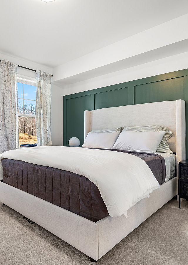 Bright and inviting bedroom with a modern upholstered bed, chic nightstand, and natural light streaming in through large windows with scenic outdoor views.