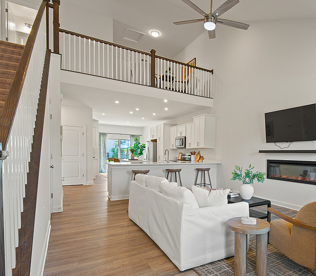 Contemporary open-concept living room with high ceilings, stylish fireplace, and sleek kitchen island, featuring modern decor and warm wood floors.