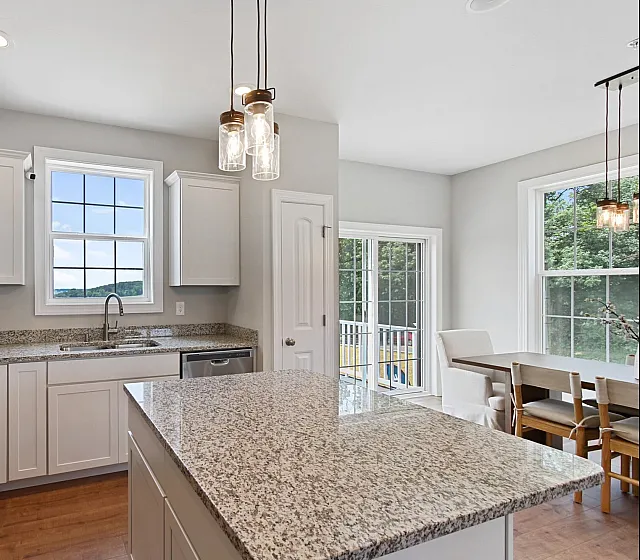 Bright and modern kitchen with white cabinets, granite countertops, and a cozy dining area with large windows overlooking greenery.