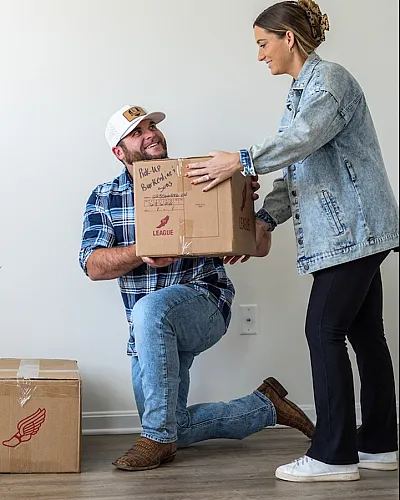 Happy couple moving into a bright and spacious apartment, unpacking boxes on polished hardwood floors.