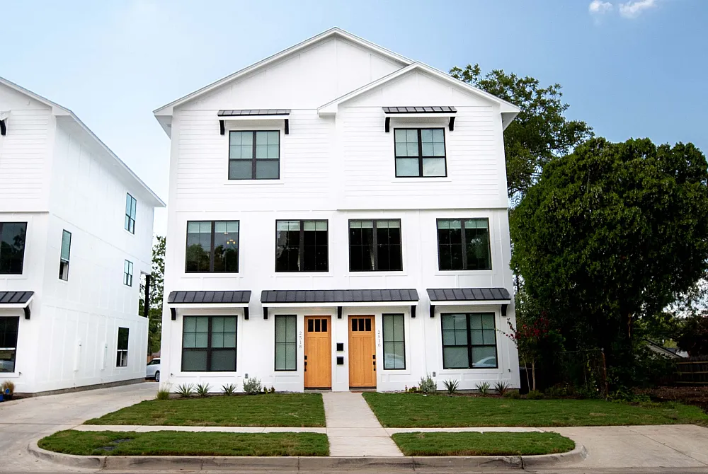 Charming modern duplex with elegant white exterior and inviting front entry, set against a picturesque blue sky.