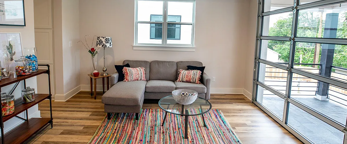 Chic living room with a cozy gray sectional sofa, colorful striped rug, and large glass garage door opening to a balcony with a serene view.