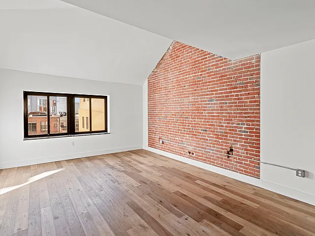 Chic apartment room featuring stylish red brick accent wall, large window with city view, and elegant hardwood floors.