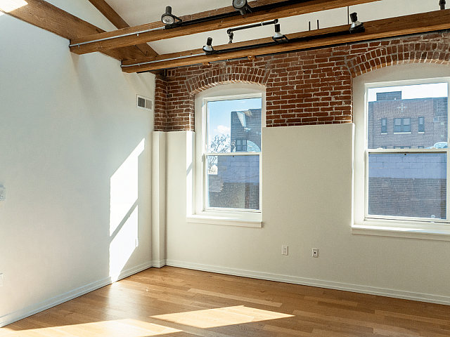 Charming loft apartment with exposed brick, rustic wooden beams, and large sunlit windows.