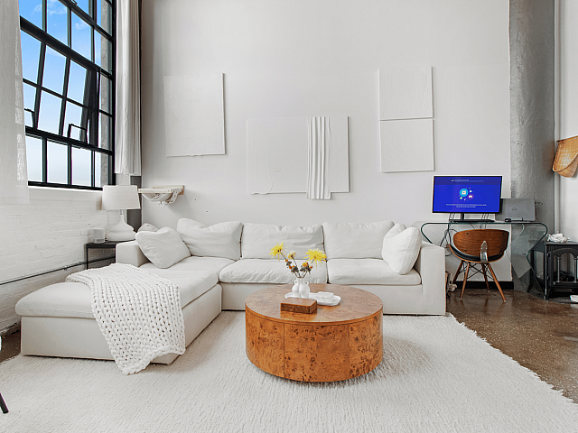 Contemporary living room with a plush white sectional, large industrial windows, stylish wall art, and a modern workspace.