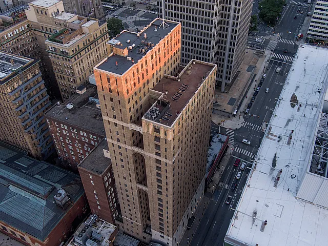 Aerial view of an elegant high-rise apartment building with sunlit architecture, offering urban living in a vibrant cityscape.