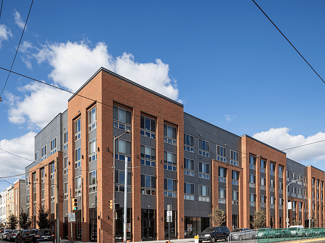 Modern urban apartment complex with stylish brick and gray facade under a clear blue sky, offering sophisticated city living.