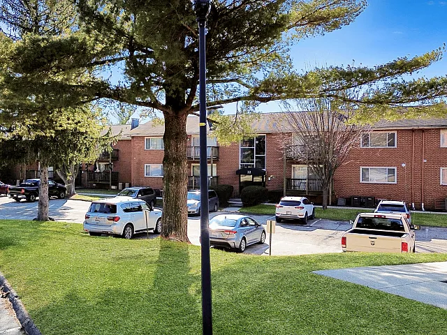 Charming brick apartment complex surrounded by lush greenery and ample parking, offering a peaceful residential setting.