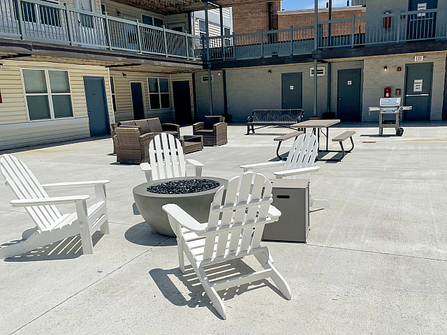 Inviting outdoor courtyard with comfortable Adirondack chairs around a modern fire pit, surrounded by cozy seating and a barbecue area for entertaining.
