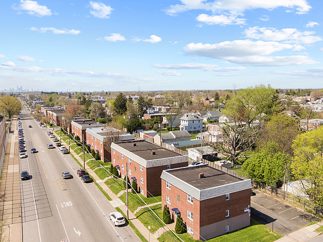 Charming suburban neighborhood with lush greenery and modern brick apartment buildings under a bright blue sky.