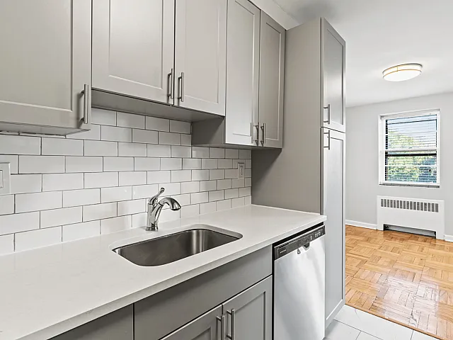 Contemporary kitchen with sleek grey cabinets, elegant white subway tiles, and natural light from a large window.