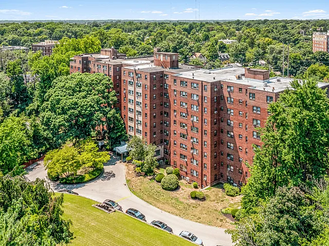 Charming aerial view of a brick apartment complex surrounded by lush greenery, offering serene living with convenient access to urban amenities.