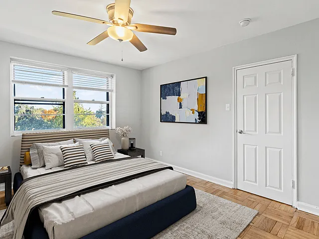 Bright and inviting bedroom with large windows, elegant ceiling fan, and tasteful modern artwork.