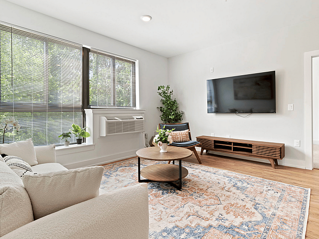 Bright and modern living room with large windows, elegant decor, and a wall-mounted TV, complemented by lush greenery and cozy seating.