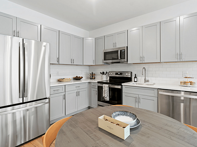 Elegant kitchen with sleek stainless steel appliances, modern grey cabinetry, and a chic wooden dining table, perfect for culinary enthusiasts.