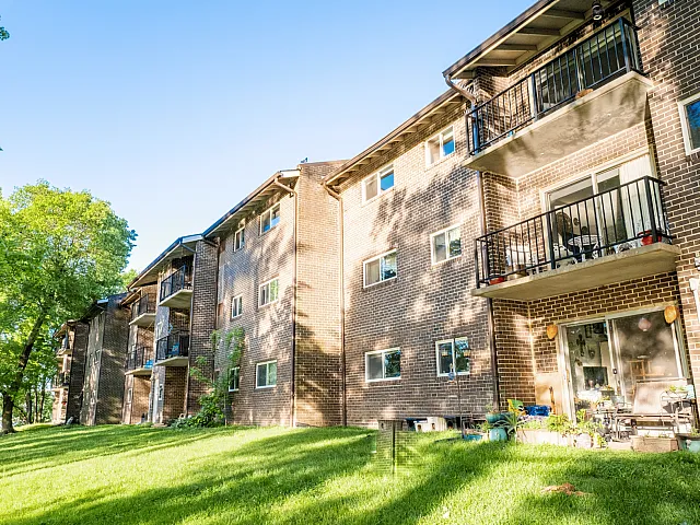Charming brick apartment building with private balconies and lush green surroundings, offering a peaceful and inviting atmosphere.