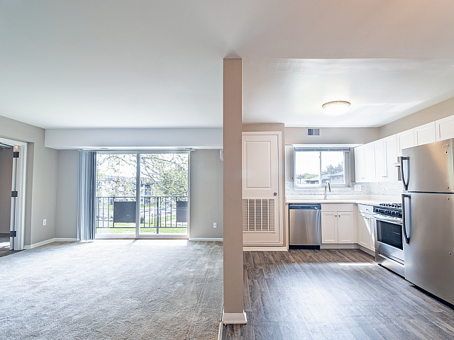 Bright apartment interior showcasing a spacious open-plan design with a sleek modern kitchen and a sunlit living area, leading to a scenic balcony view.