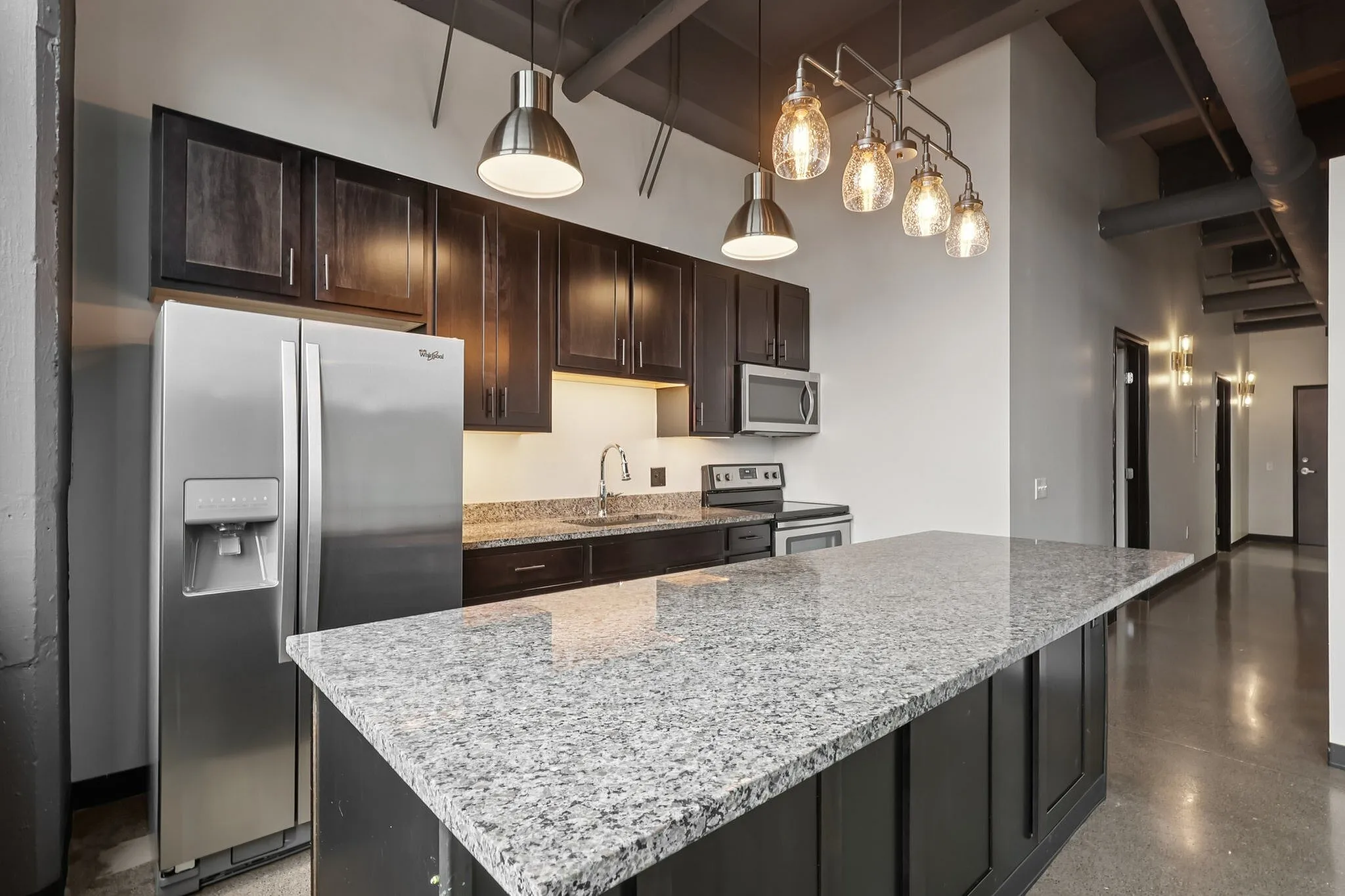 Modern kitchen with sleek granite countertops, stainless steel appliances, and elegant pendant lighting, offering a stylish and functional space.