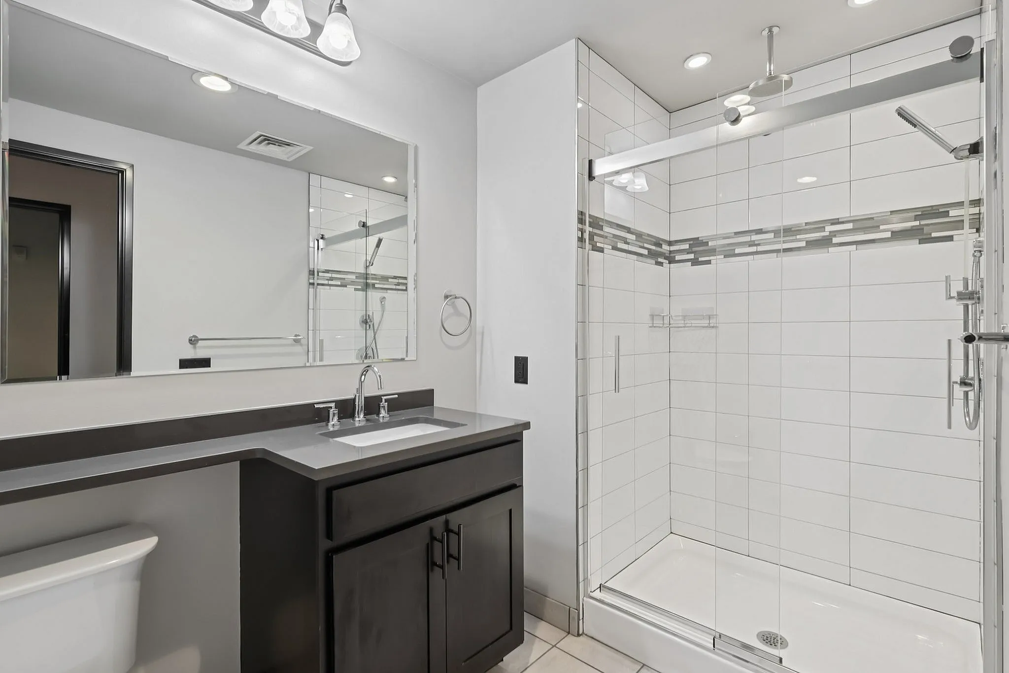 Elegant bathroom featuring a sleek glass walk-in shower, modern vanity with large mirror, and stylish tile accents.