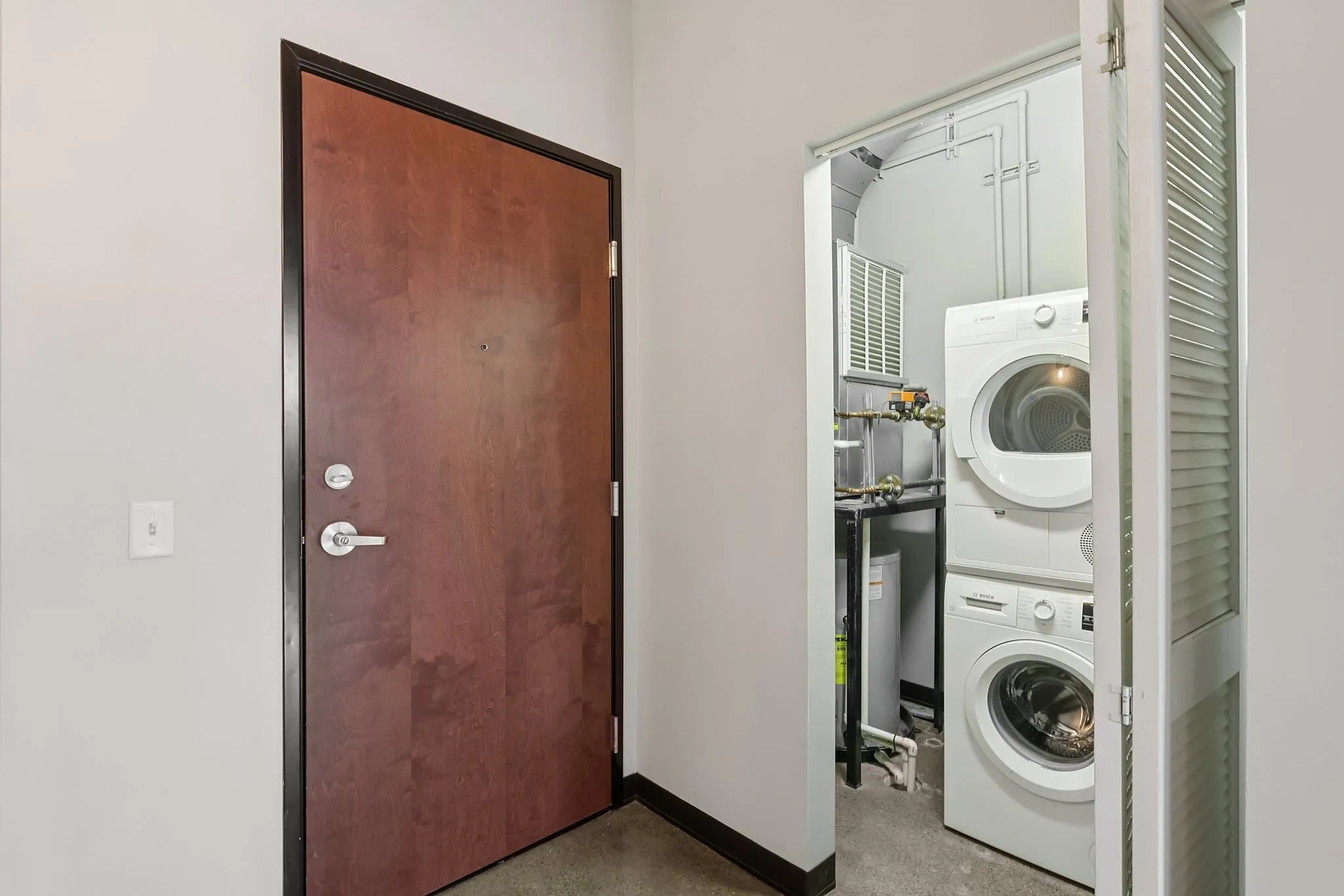 Modern apartment entryway featuring a sleek wooden door and a convenient in-unit washer and dryer.