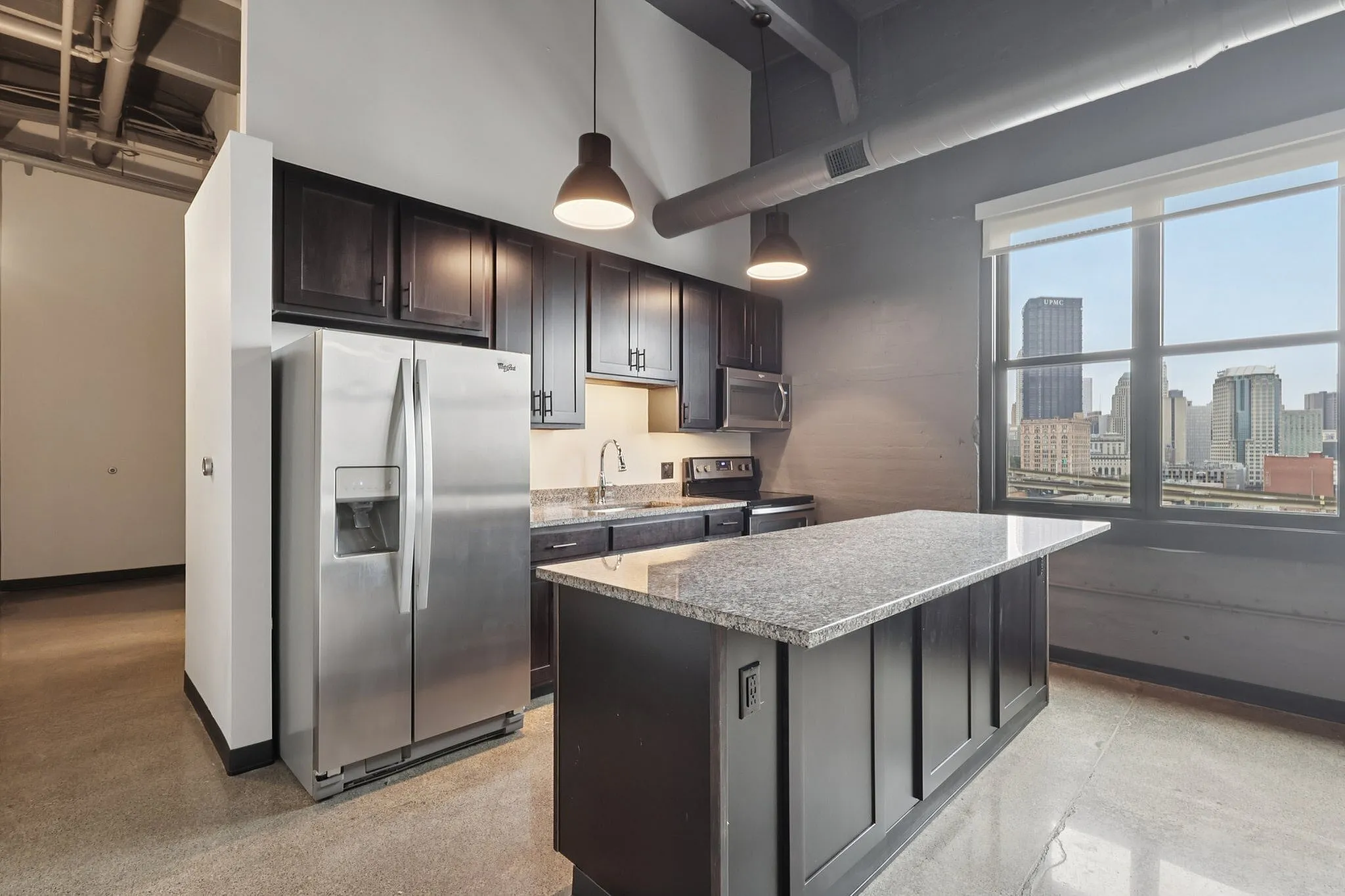 Modern apartment kitchen with sleek dark cabinetry, granite countertops, and panoramic city views from large window.