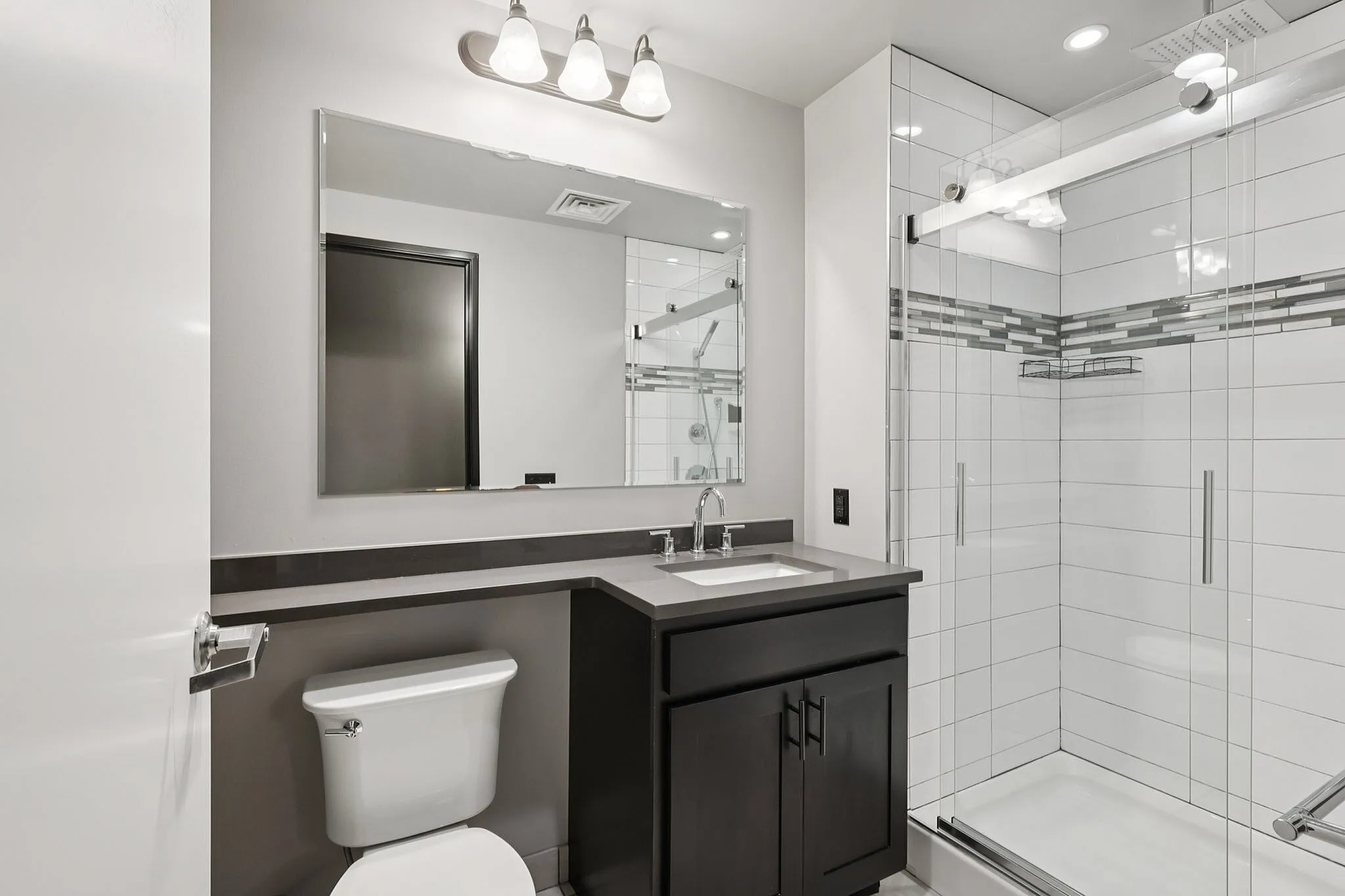 Modern bathroom with sleek glass shower, elegant dark vanity, and bright lighting creating a luxurious atmosphere.
