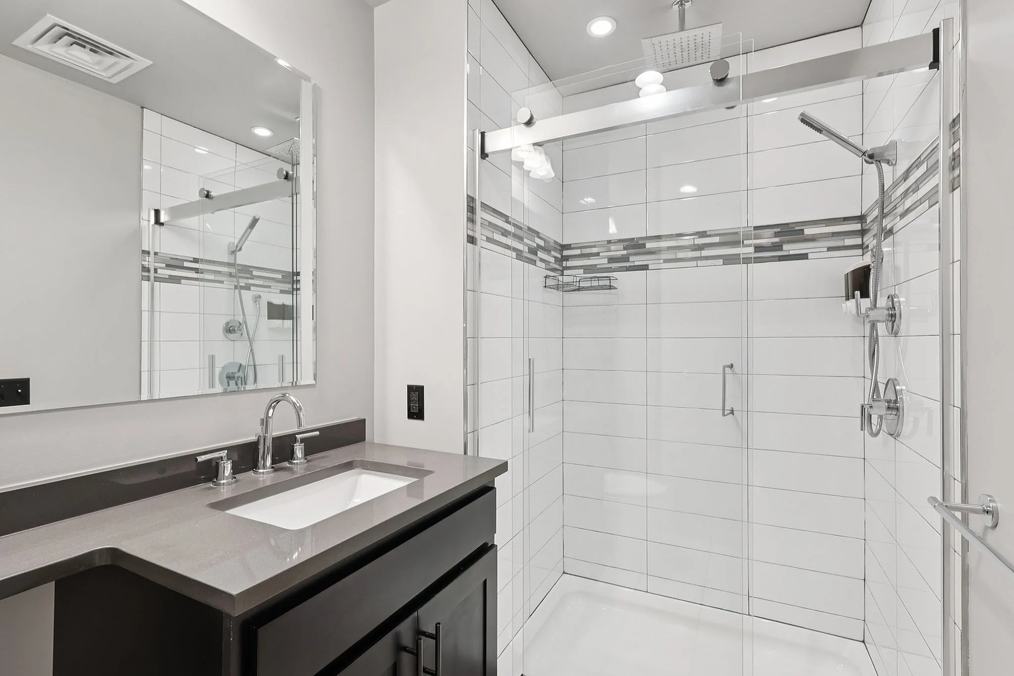 Modern bathroom with sleek gray countertop, stylish faucet, and glass-enclosed rainfall shower.