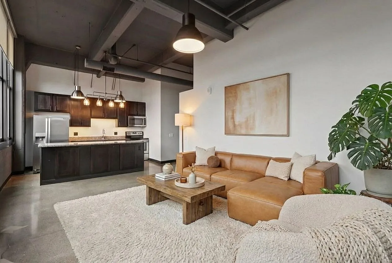 Chic industrial-style open living space featuring a cozy leather sectional, elegant wooden accents, and a modern kitchen with sleek stainless steel appliances.