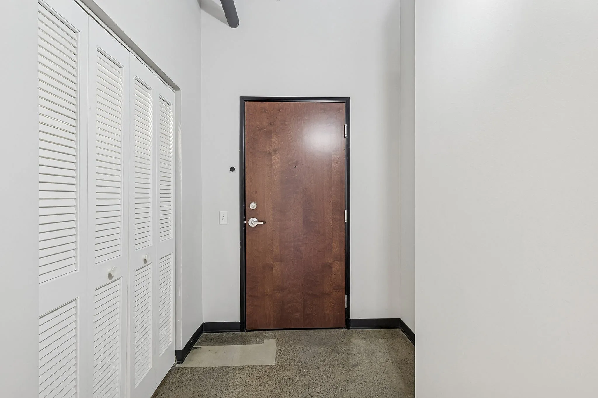 Inviting apartment entrance showcasing a sleek wooden door with modern white closet doors, creating a welcoming and stylish atmosphere.