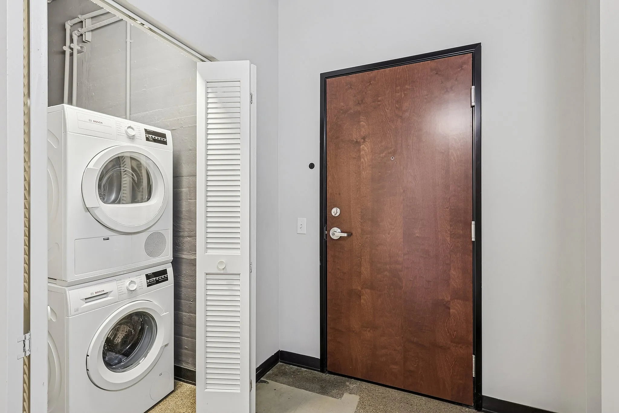 Modern entryway featuring a convenient in-unit stacked washer and dryer next to a sleek wooden door.