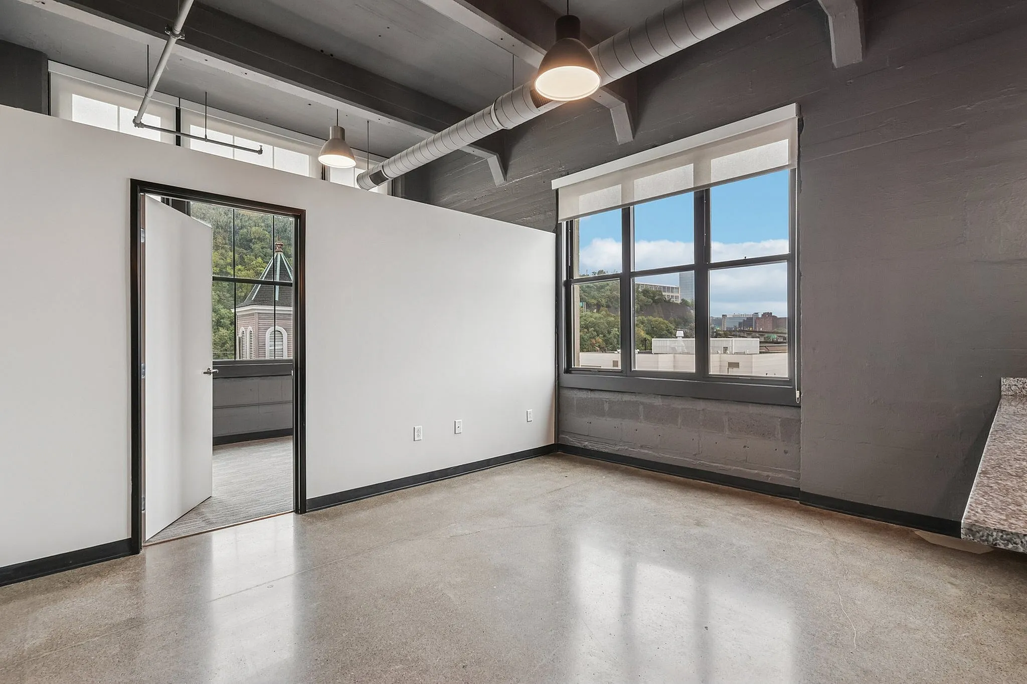 Chic industrial-style apartment with polished concrete floors, large window offering cityscape views, and exposed ductwork for a modern urban vibe.