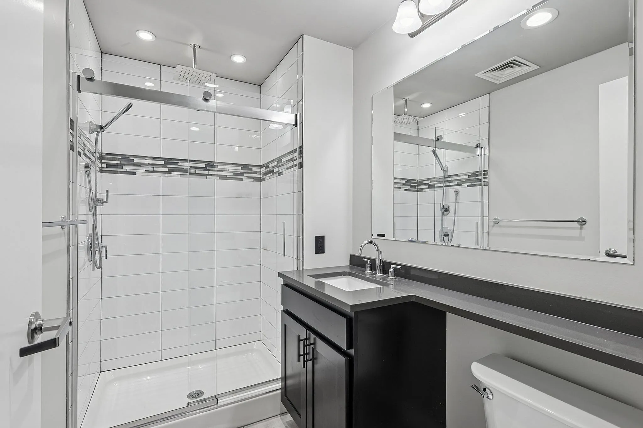 Modern bathroom with sleek glass shower, elegant white tiles, dark vanity, and upscale fixtures.