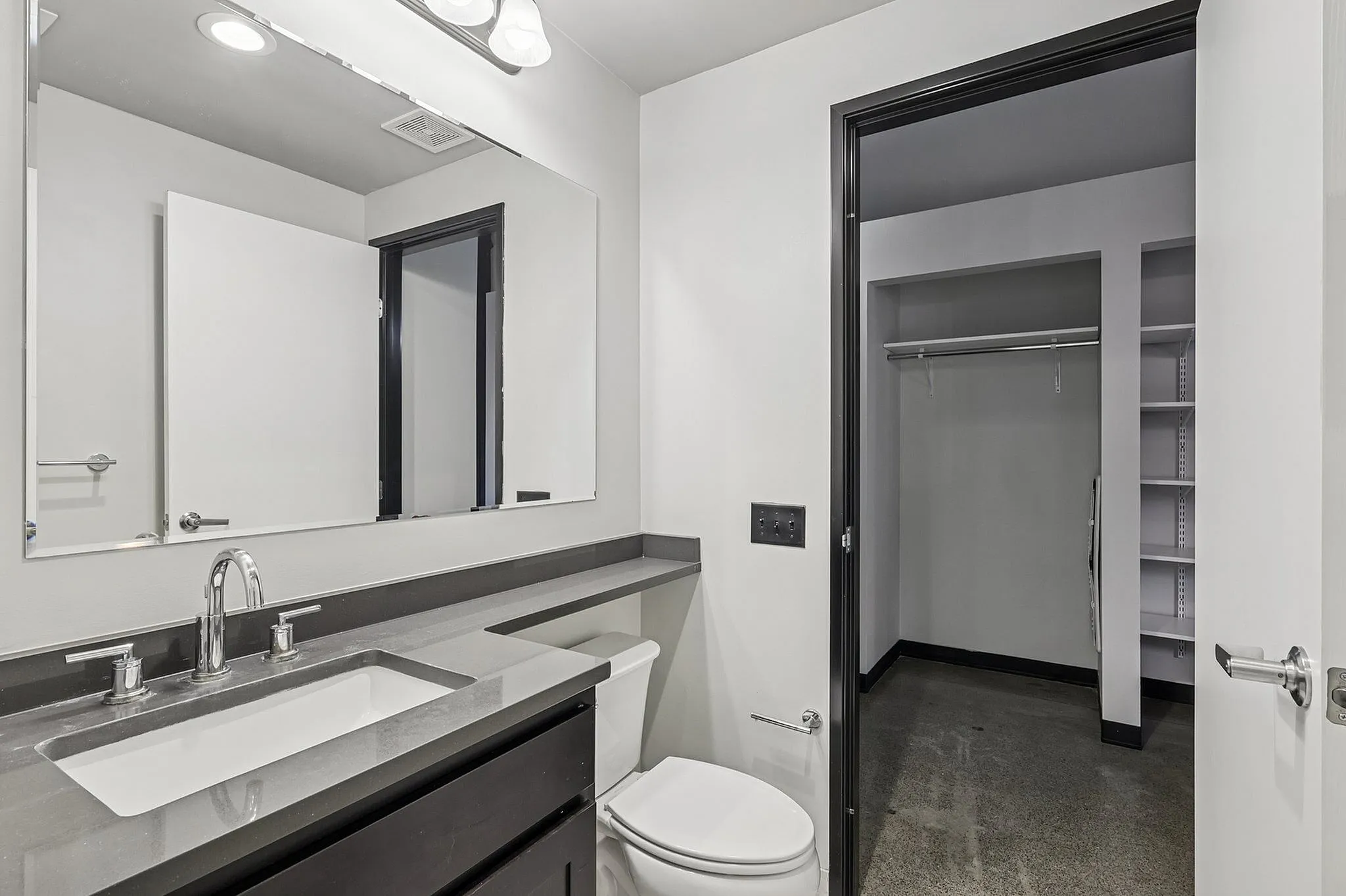 Modern bathroom featuring sleek fixtures, spacious vanity, and adjacent walk-in closet for ample storage.