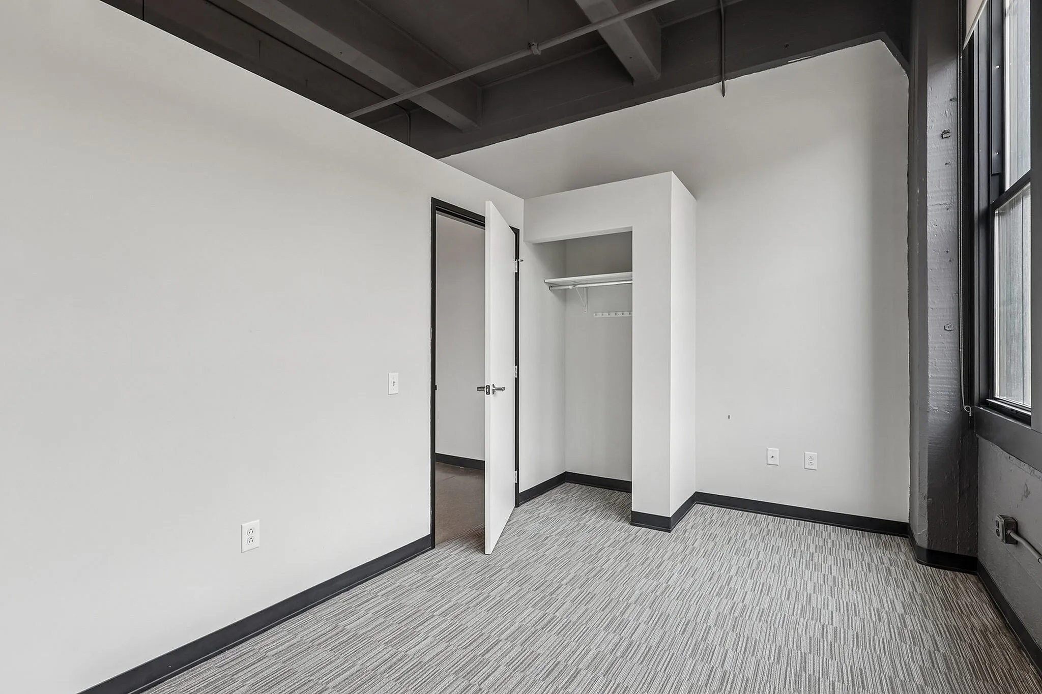 Modern apartment interior with open closet, neutral tones, and large window providing natural light.