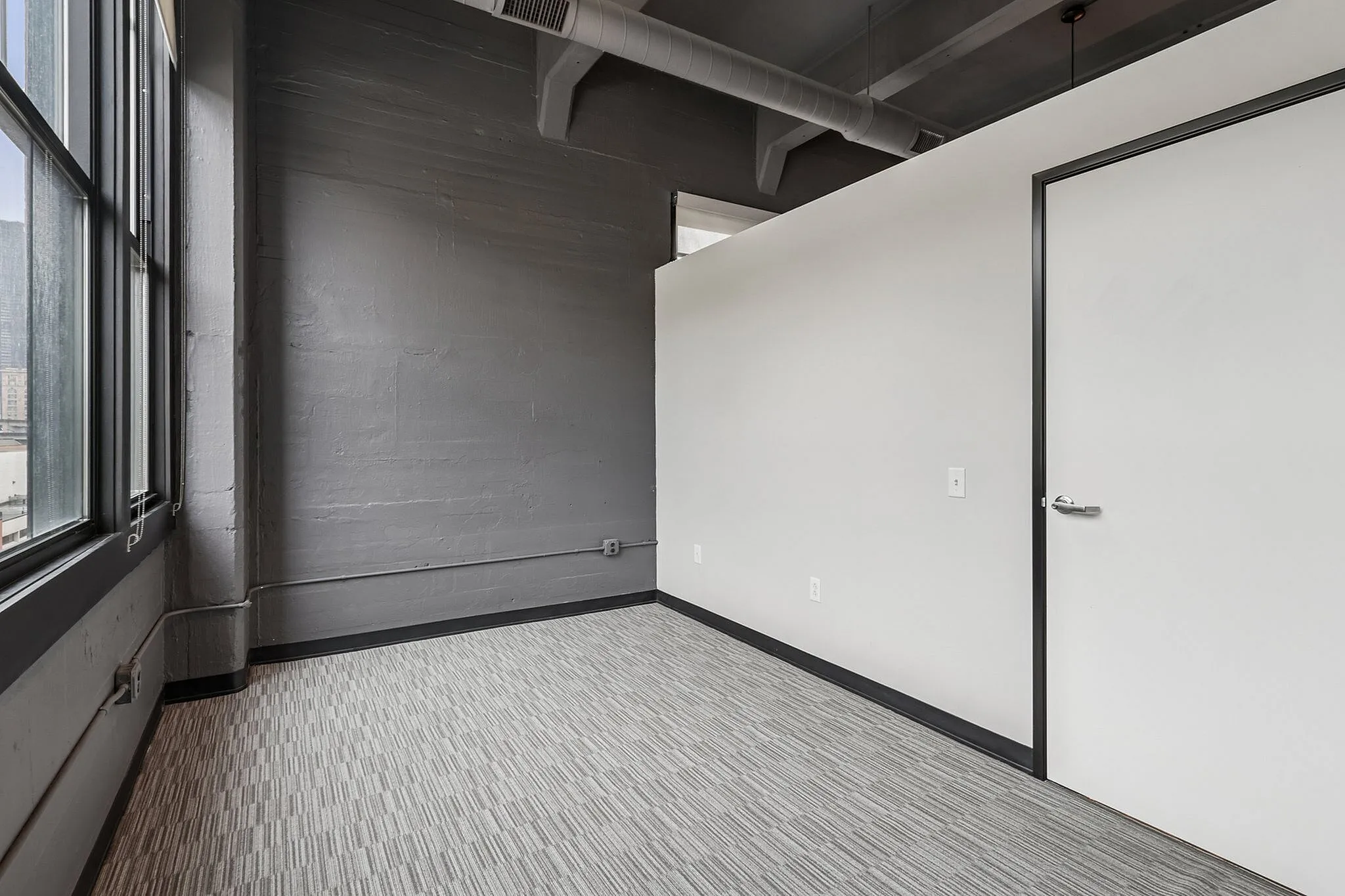 Bright, industrial-style room with large windows, sleek grey walls, and modern carpeting.