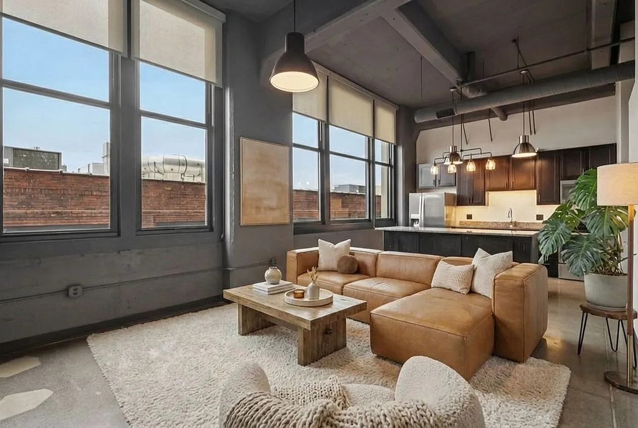 Modern urban loft with open-concept design, featuring a stylish living area, plush leather sectional, and sleek kitchen with industrial lighting.