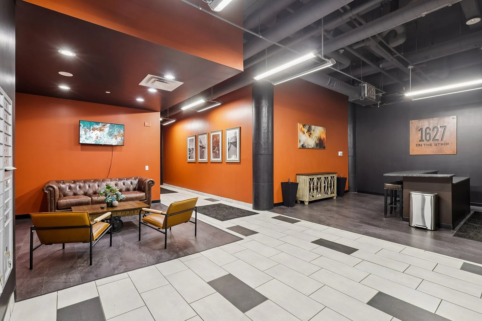 Modern lobby with vibrant orange walls, stylish seating area, and artistic decor at '1627 on the Strip'.