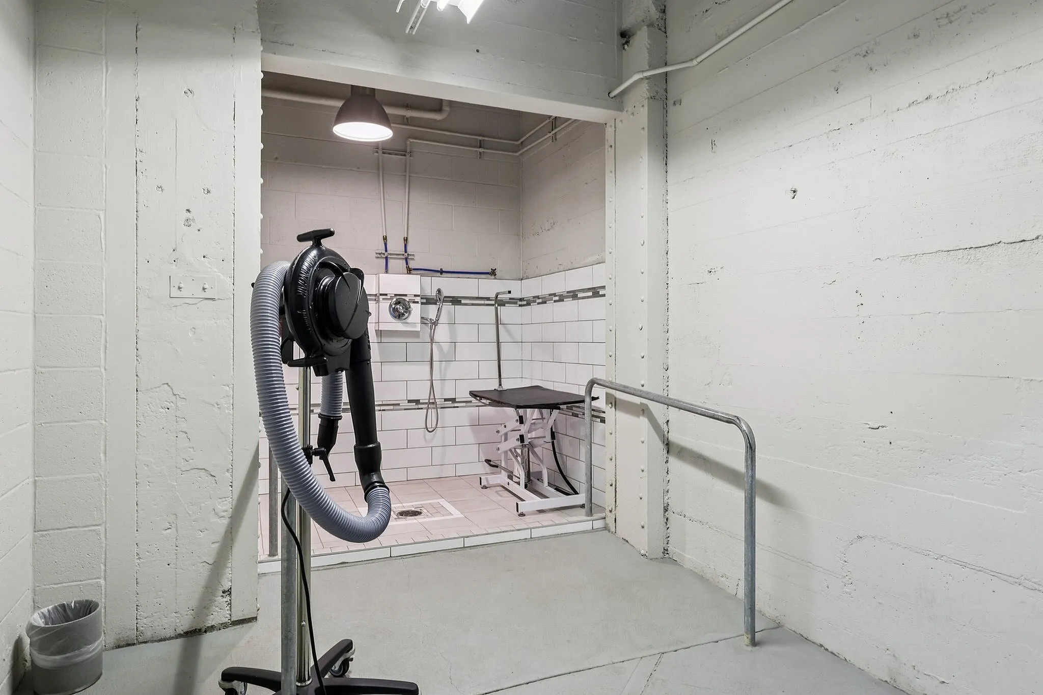 Modern utility room with white tiled walls, equipped with a professional dryer and a stainless steel shower setup, ideal for versatile use.