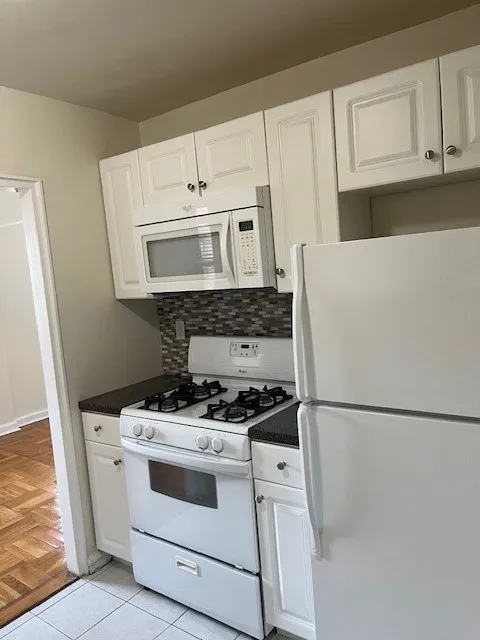 Modern kitchen with white cabinets, a full-size refrigerator, gas stove, and built-in microwave in a cozy apartment setting.