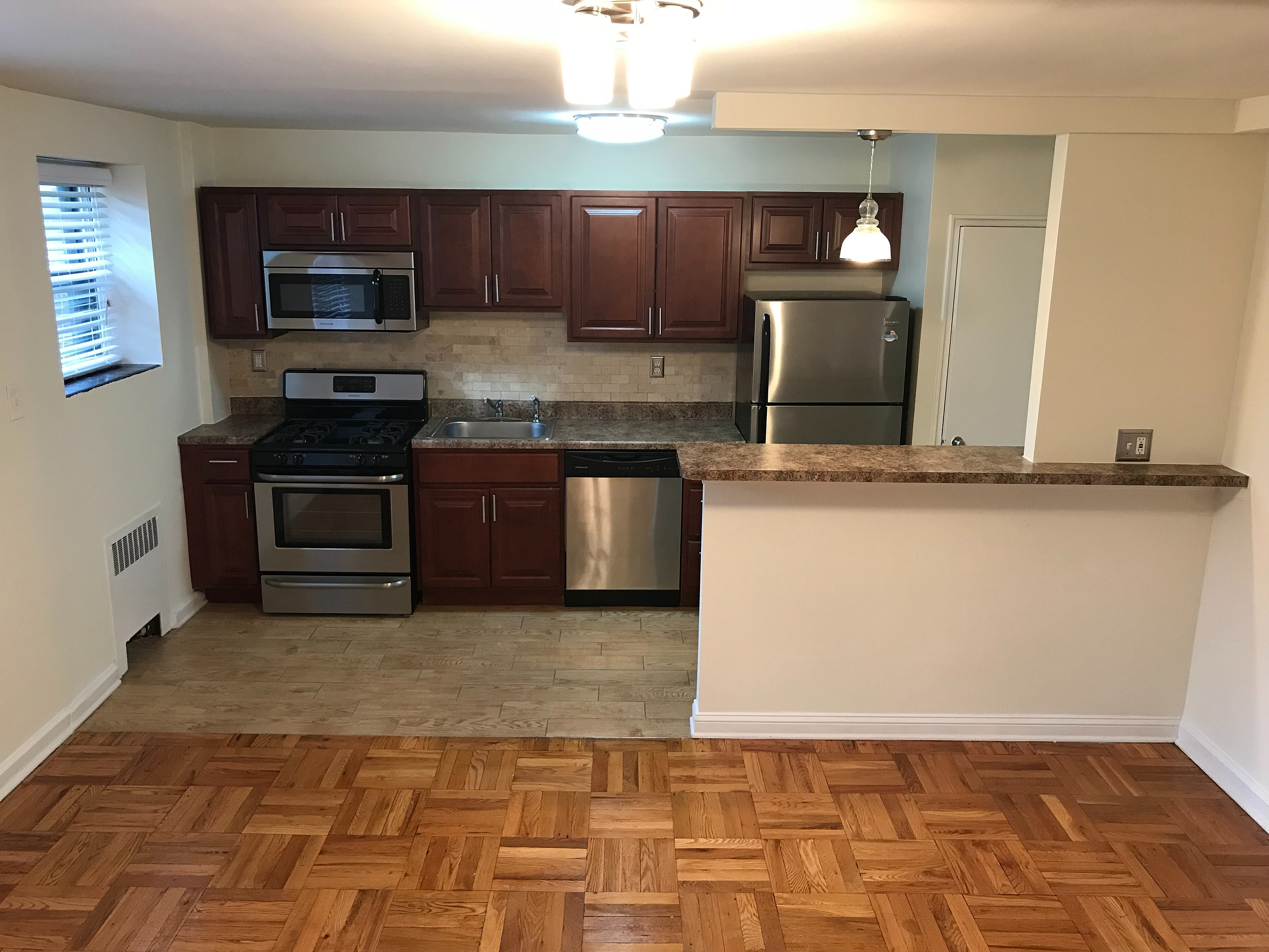 Charming modern kitchen with rich wood cabinetry, stainless steel appliances, and granite countertop overlooking open parquet living area.