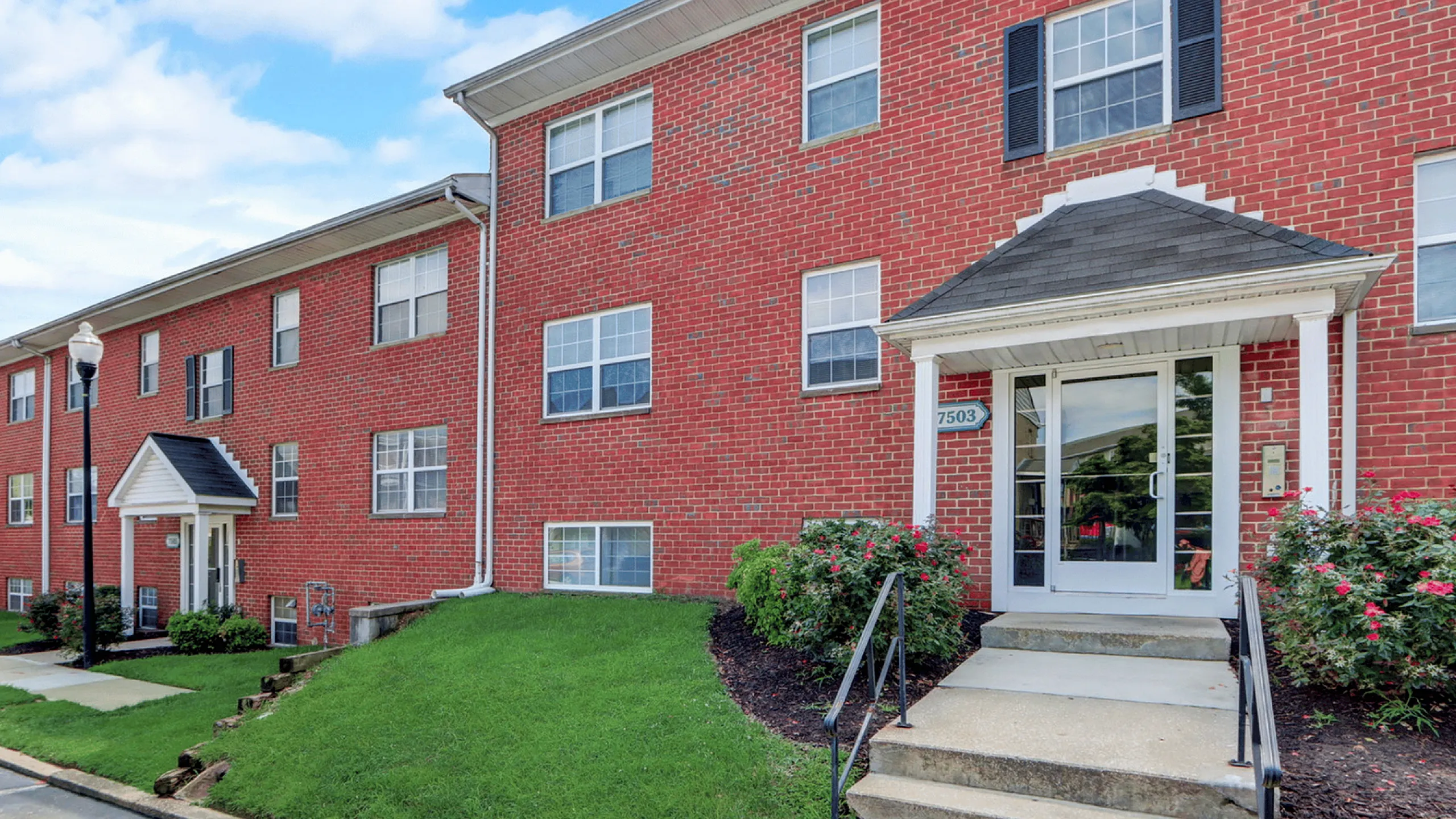 Charming brick apartment building with lush greenery and inviting entrance.
