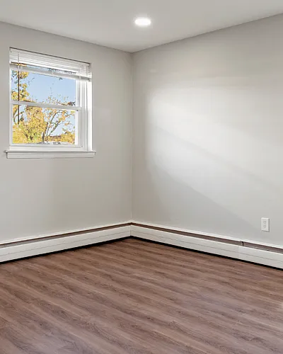 Spacious room with large windows, natural light, and elegant wooden flooring.