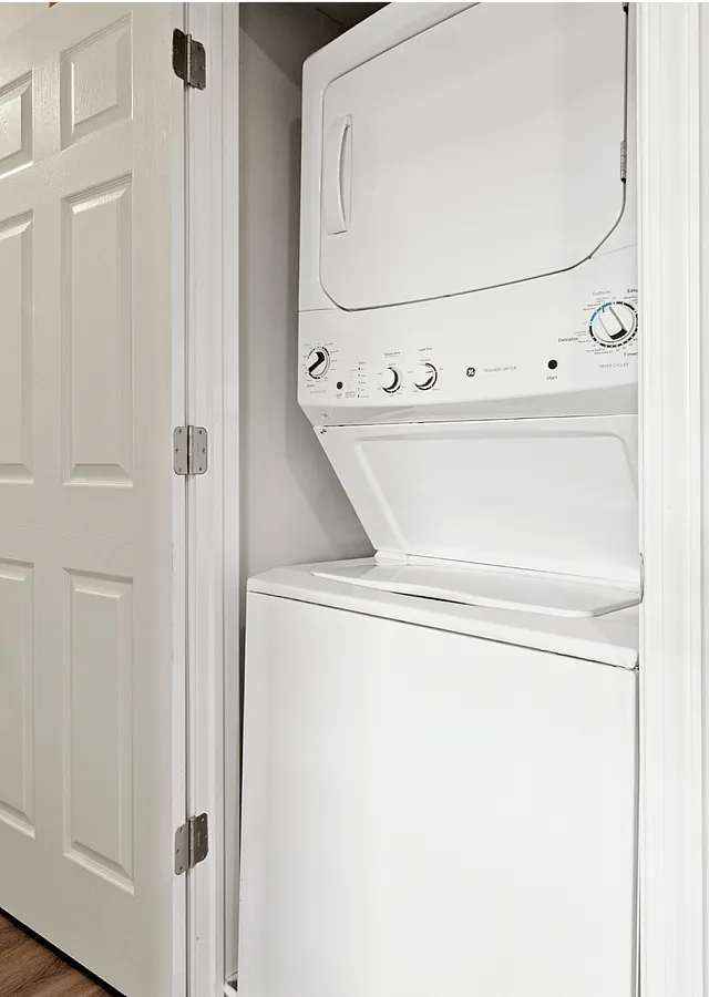 Hallway with a stylish in-unit stacked washer and dryer next to bright living spaces.