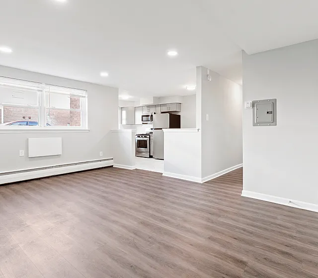 Bright open-concept living space with hardwood floors, large window, and adjacent kitchen featuring stainless steel appliances.