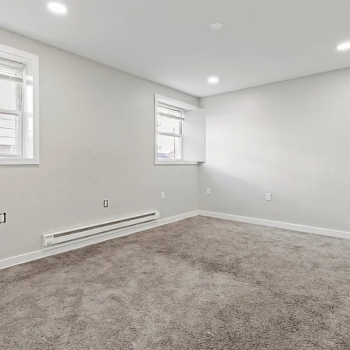 Inviting empty room with soft carpet flooring and large windows letting in natural light.